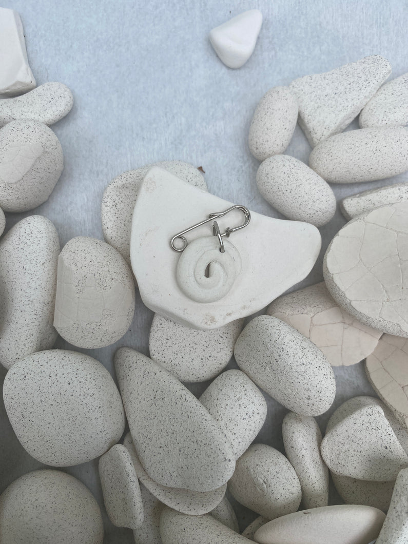 Close-up of a spiral pin on a white stone among pebbles